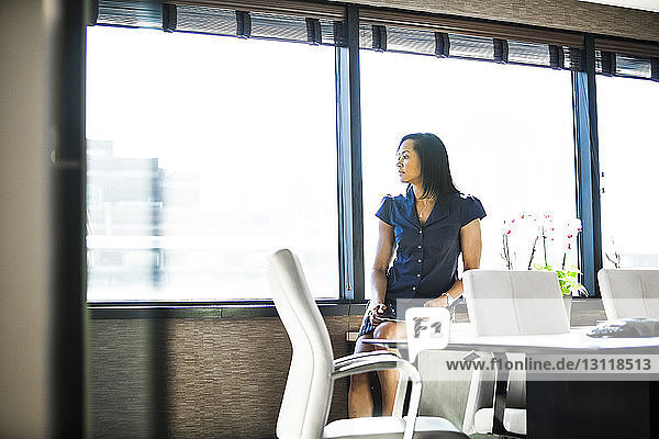 Nachdenkliche Geschäftsfrau schaut durch das Fenster  während sie im Büro sitzt