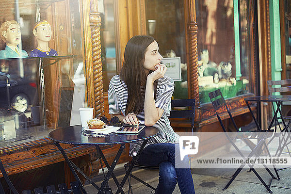 Nachdenkliche Frau sitzt an sonnigen Tagen am Tisch im Straßencafé