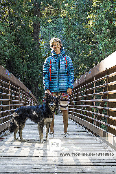 Porträt eines glücklichen Mannes mit Hund auf einem Steg im Wald stehend