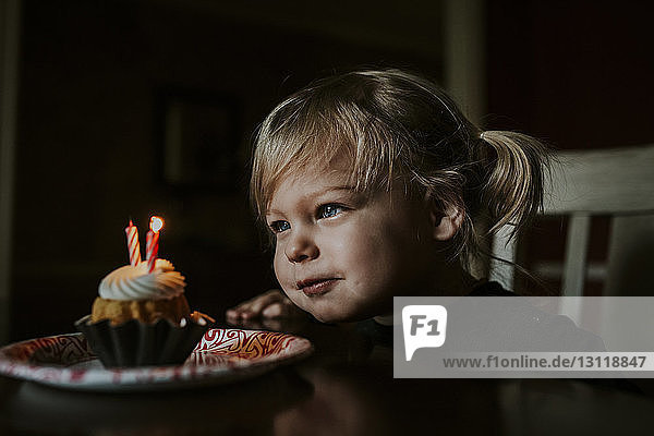 Süßes Mädchen schaut auf ihren Geburtstagskuchen auf dem Tisch
