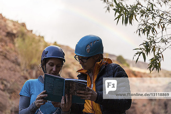 Hikers wearing helmets while reading guidebook against mountains