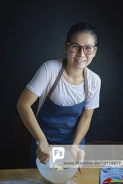 Porträt einer lächelnden Frau  die in der Küche Teig in einer Schüssel rührt