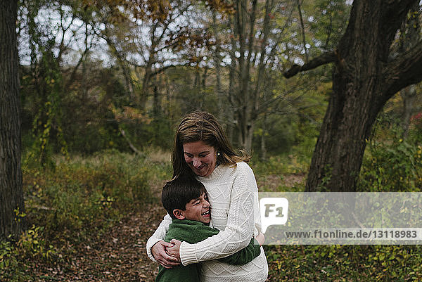 Happy mother embracing son while standing on field at park