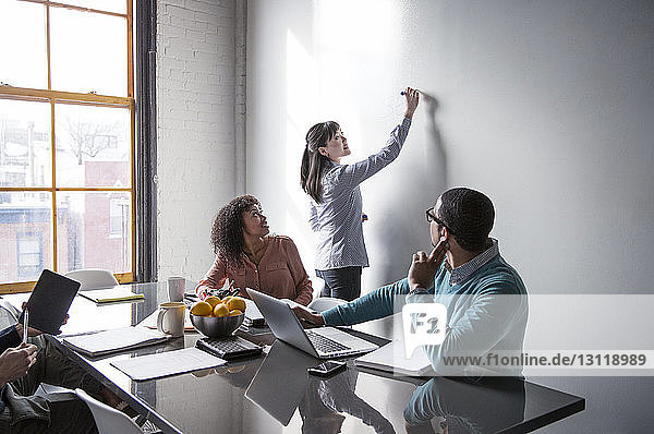 Male and female colleagues looking at businesswoman writing on whiteboard
