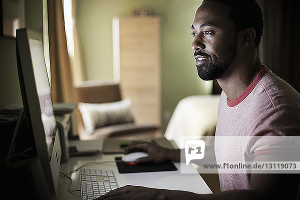 Lächelnder Mann benutzt Computer  während er zu Hause sitzt