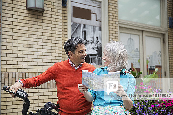 Glückliches reifes Paar liest Straßenkarte  während es mit dem Fahrrad vor dem Gebäude steht