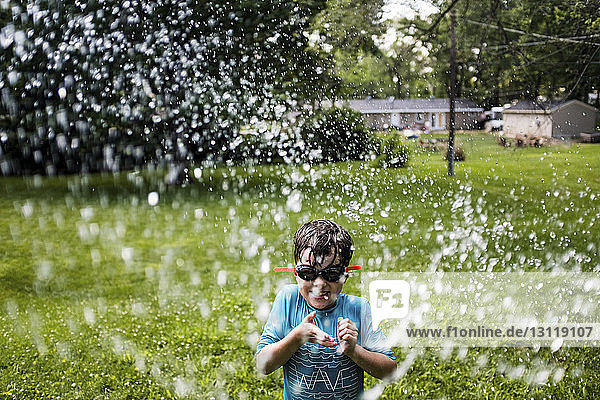 Verspielter Junge mit Schwimmbrille beim Spielen mit Wasser im Hof