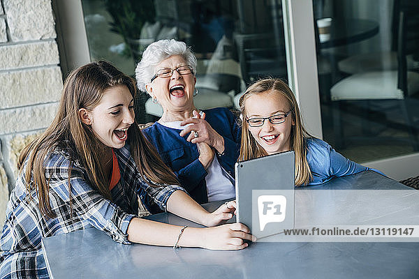Hochwinkelansicht von glücklichen Enkelinnen und Großmüttern mit Tablet-Computer auf der Veranda