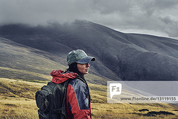 Side view of female hiker with backpack standing on Balkan Mountains against cloudy sky