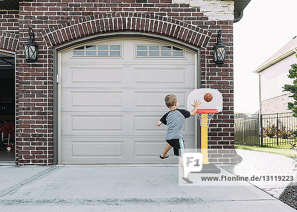 Glücklicher Junge wirft Ball im Basketballkorb auf Einfahrt