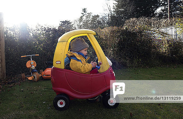 Mädchen fährt Spielzeugauto auf Grasfeld im Hinterhof