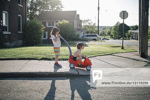Geschwister spielen mit Spielzeugauto auf Fußweg gegen den Himmel