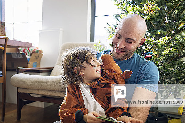Glücklicher Vater betrachtet kostümierten Sohn zu Hause am Weihnachtsbaum