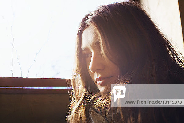 Thoughtful woman sitting by window on sunny day