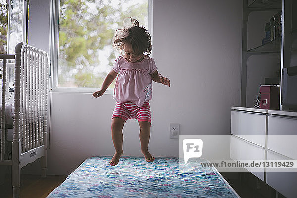 Cheerful girl jumping on bed at home