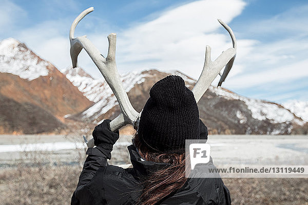 Rückansicht einer Frau  die im Denali-Nationalpark ein Geweih gegen die Berge hält