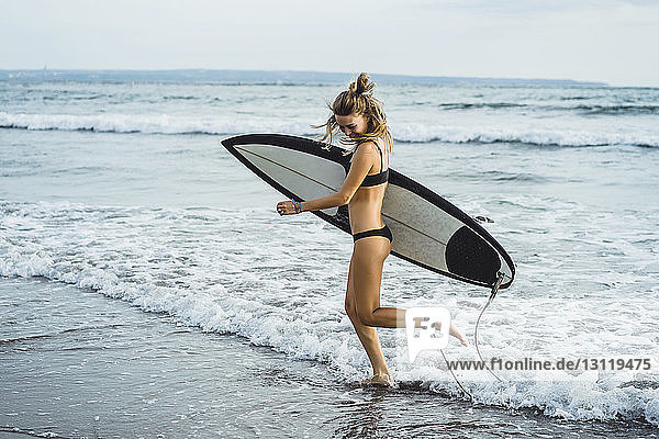 Side view of woman carrying surfboard while walking on shore at beach