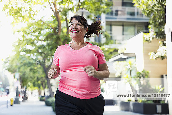 Cheerful woman jogging on footpath in city