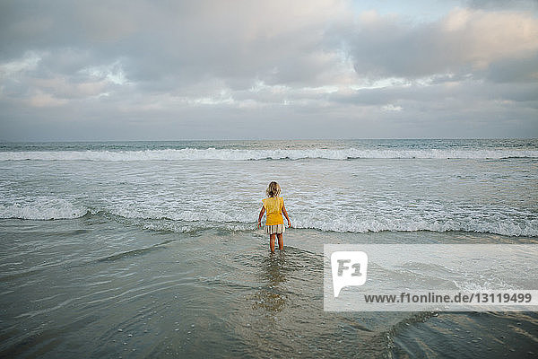 High angle view of carefree girl standing in sea at beach against cloudy sky