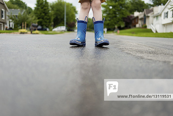 Niedriger Teil eines Jungen in Gummistiefeln auf nasser Straße stehend