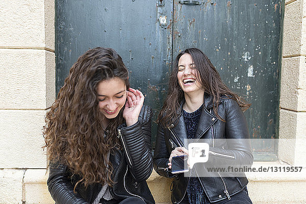 Glückliche Freunde benutzen ein Smartphone  während sie an der Tür sitzen