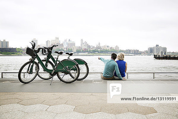 Rear view of mature couple sitting by bicycles at observation point in city