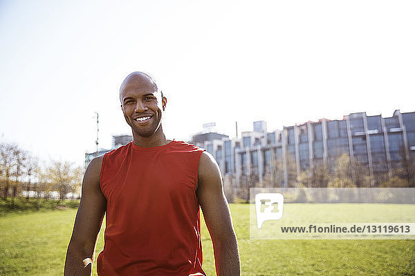 Porträt eines lächelnden männlichen Athleten  der auf einem Grasfeld in der Stadt steht