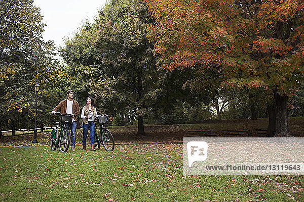 Couple talking while walking with bicycles in park