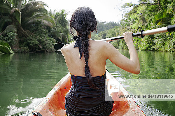 Rückansicht einer Kajak fahrenden Frau auf einem See im Wald