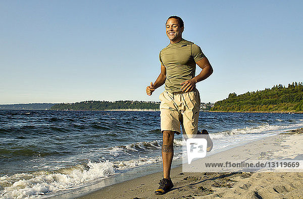 Cheerful man jogging on shore against clear sky