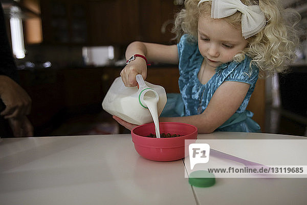 Mädchen gießt Milch in Schüssel auf den Tisch