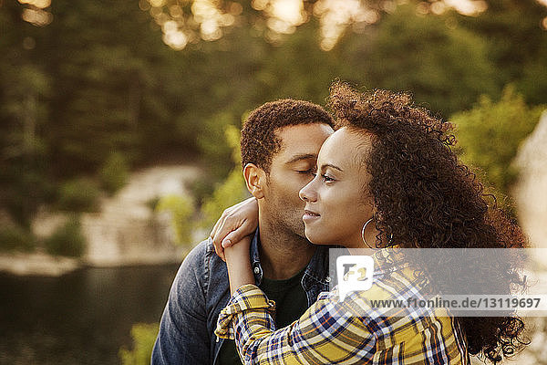 Loving man kissing woman while sitting at lakeshore during sunset
