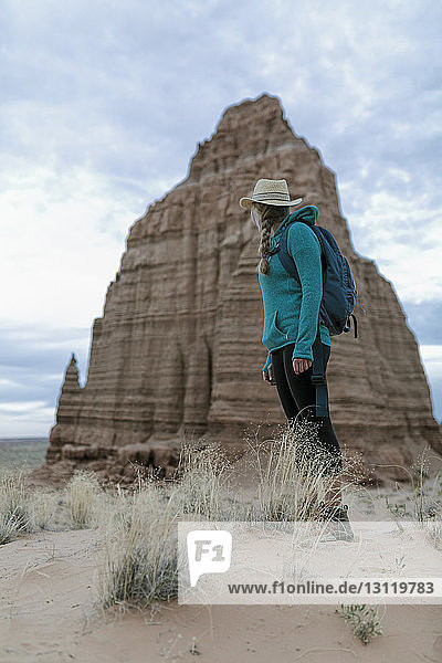 Seitenansicht einer Wanderin  die vor Felsformationen und bewölktem Himmel in der Wüste steht