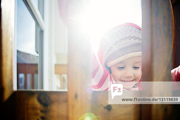 Babymädchen mit Kapuzenjacke durch Holzgeländer bei Sonnenschein gesehen