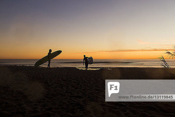 Couple carrying surfboards while walking on San Onofre State Beach during sunset