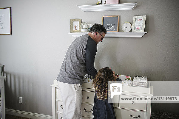 Vater und Tochter pflücken ein kleines Mädchen  das zu Hause auf einem Schrank liegt