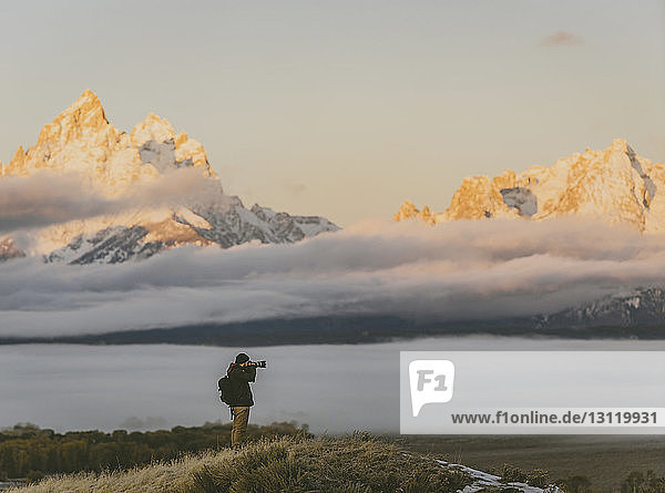 Seitenansicht eines Wanderers  der mit der Kamera fotografiert  während er an den Bergen steht