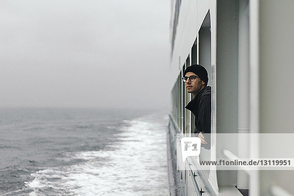 Mann schaut durch ein Fenster  während er auf einem Kreuzfahrtschiff reist