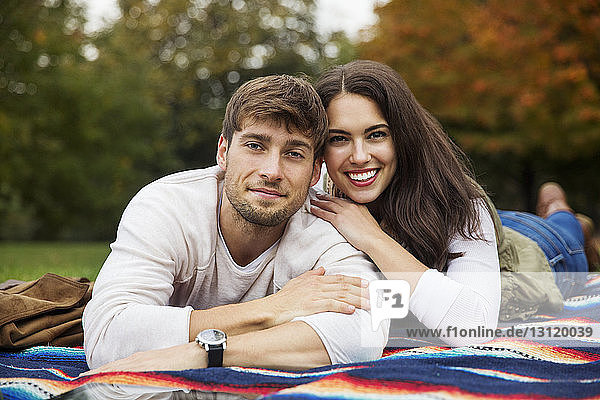 Portrait of smiling couple lying on blanket at park