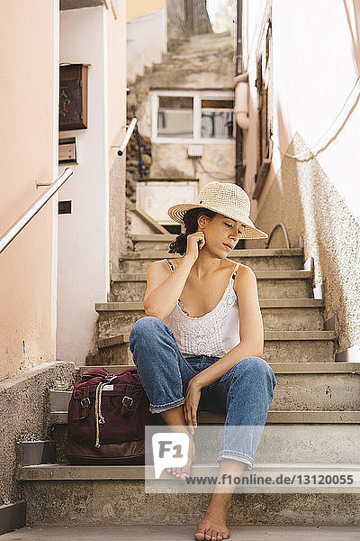 Nachdenklicher Tourist mit Hut  während er mit dem Rucksack auf Stufen in der Stadt sitzt