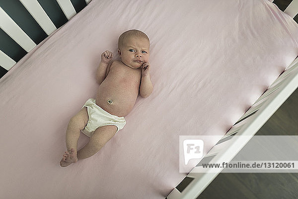 High angle portrait of shirtless baby girl lying in crib at home