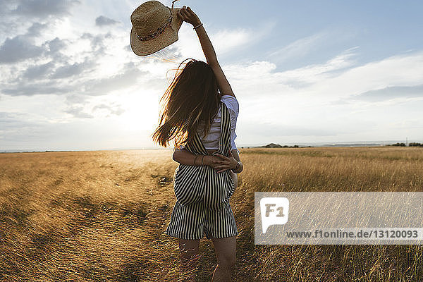 Happy woman carrying twin sister while standing on grassy field against sky during sunset
