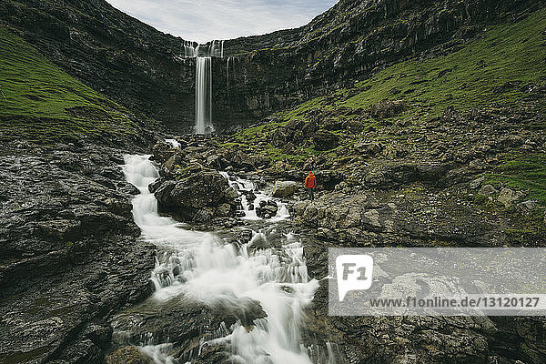 Fernansicht eines Wanderers  der auf Felsen vor einem Wasserfall steht