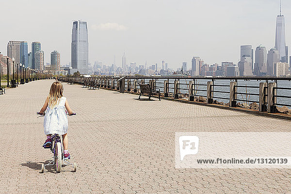 Rear view of girl cycling on promenade with city skyline in background