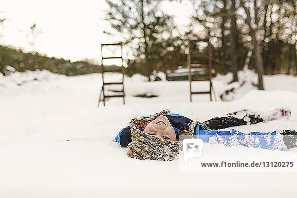 Portrait of girl winking eye while lying on snow covered field