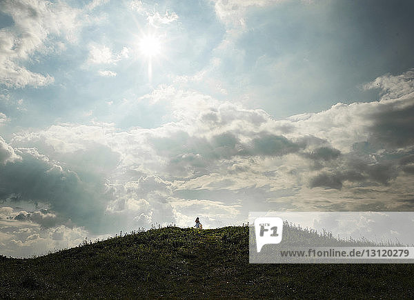 Mid distance view of girl standing on hill against cloudy sky