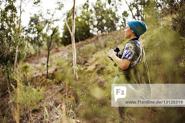 Seitenansicht einer Frau  die mit einem Fernglas in der Hand im Wald wegschaut