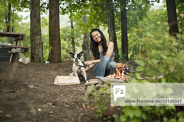 Portrait of happy woman sitting with Boston Terrier in forest