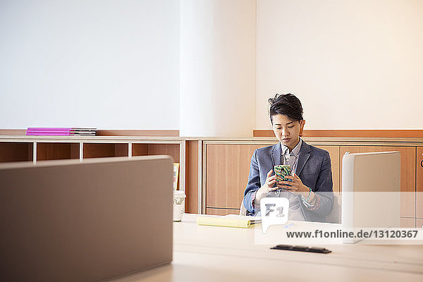 Zuversichtliche Geschäftsfrau benutzt Mobiltelefon am Tisch im Büro