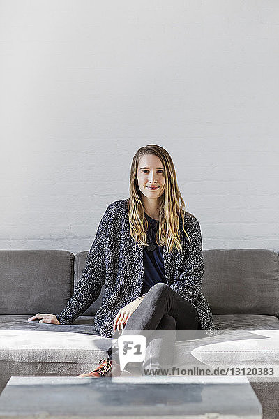 Portrait of confident businesswoman sitting on sofa against wall at office